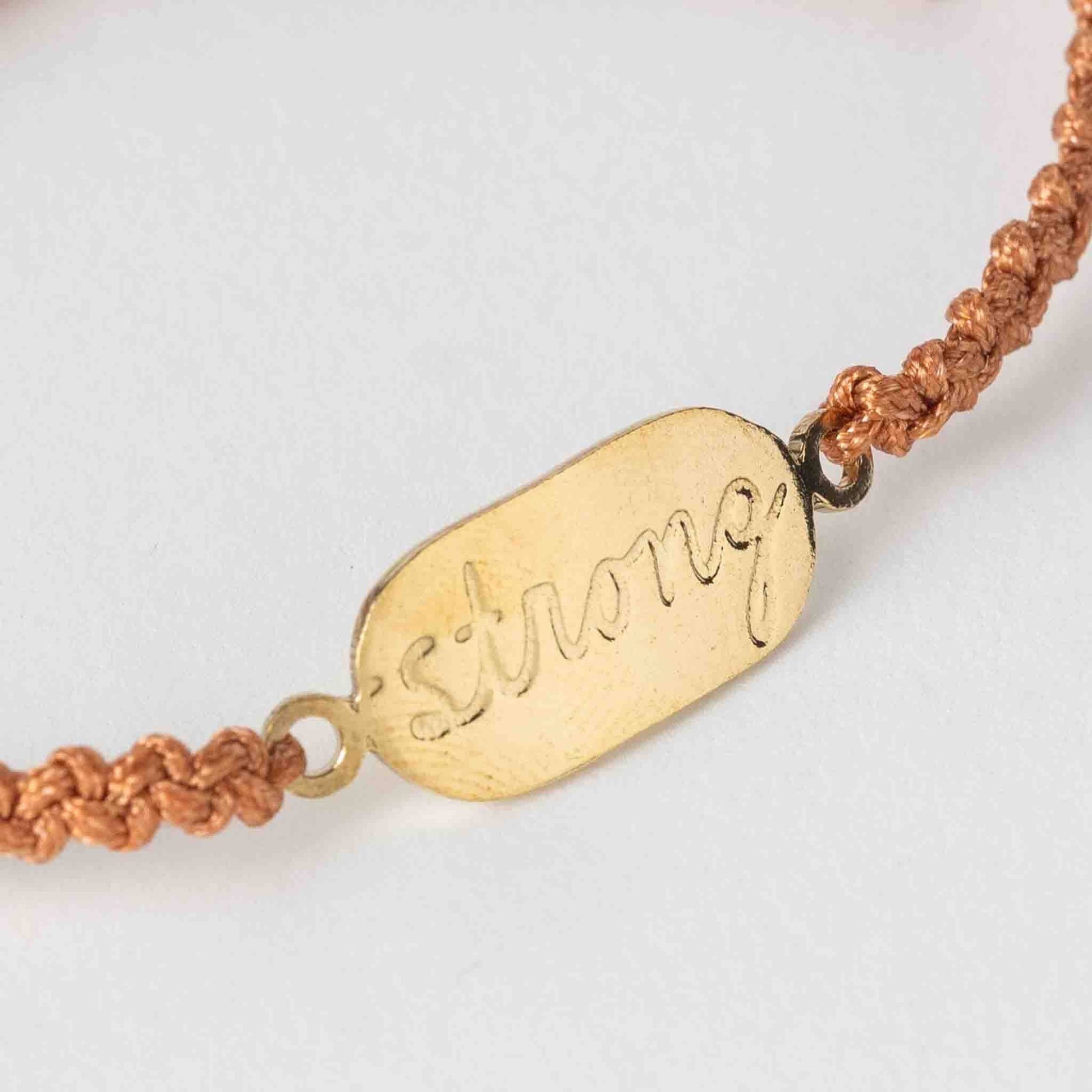 Bracelet with gold tag that says 'strong' on a white background