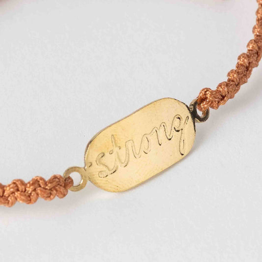 Bracelet with gold tag that says 'strong' on a white background