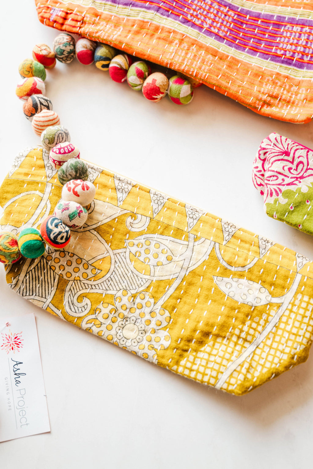 Yellow fabric pouch with floral patterns on a white surface, surrounded by decorative items.