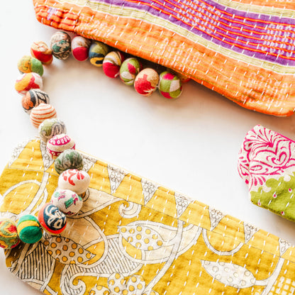 Yellow fabric pouch with floral patterns on a white surface, surrounded by decorative items.