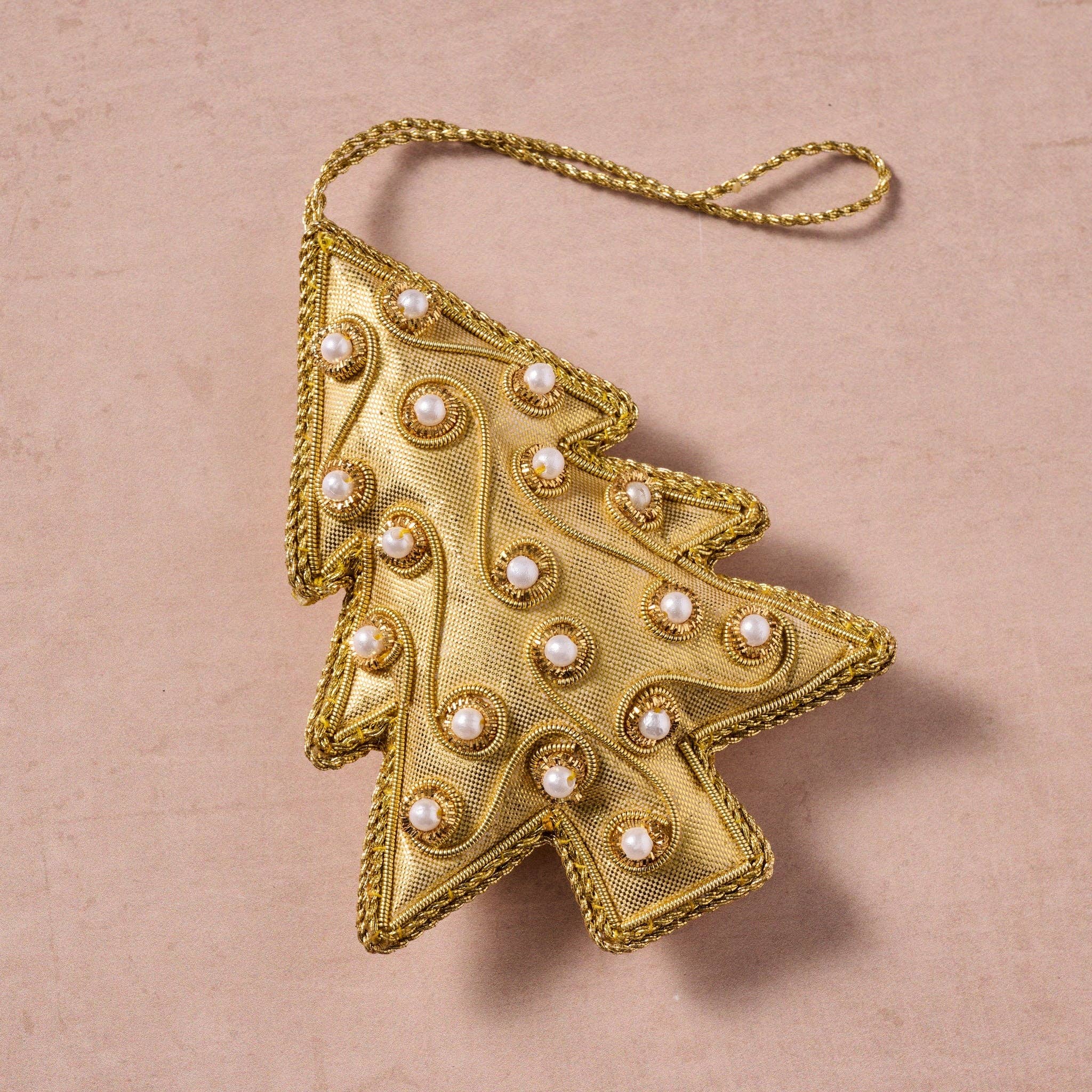 Gold Christmas tree ornament with pearl-like embellishments on a beige background
