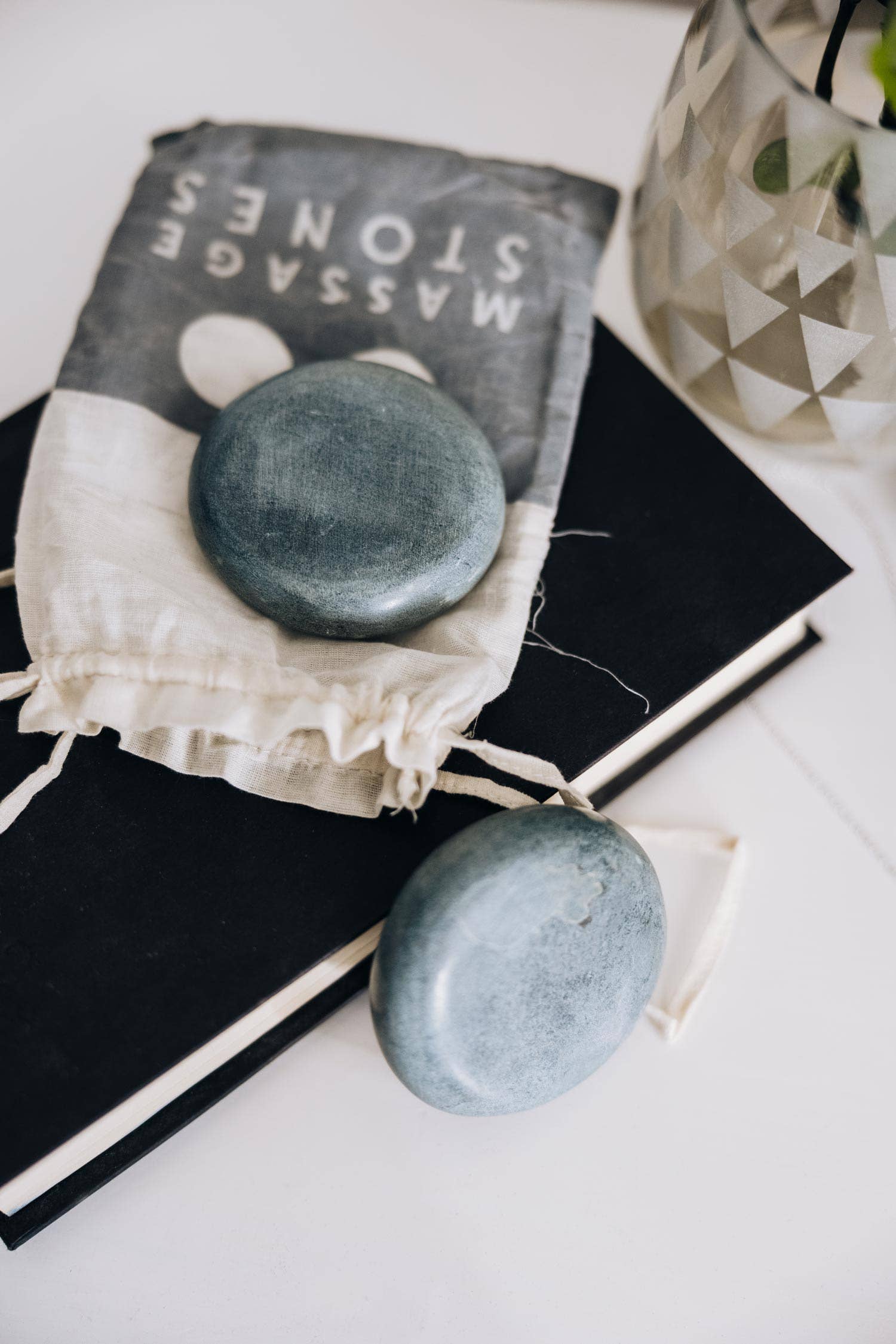 Two blue stones in a drawstring bag on top of black books with a glass container in the background.