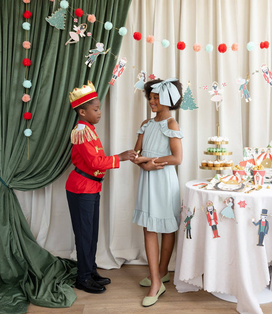 Two children in festive costumes standing in a decorated room with a table and decorations.