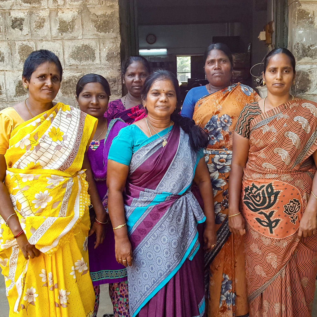 Group of women who create the soap, are in colorful sarees standing together outdoors.