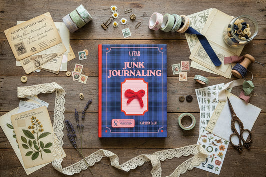 Book titled 'A Year of Junk Journaling' surrounded by vintage materials on a wooden surface