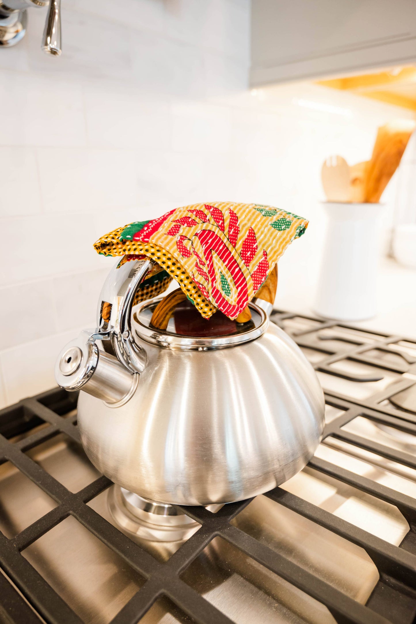Silver teapot on a stove with a colorful tea cozy