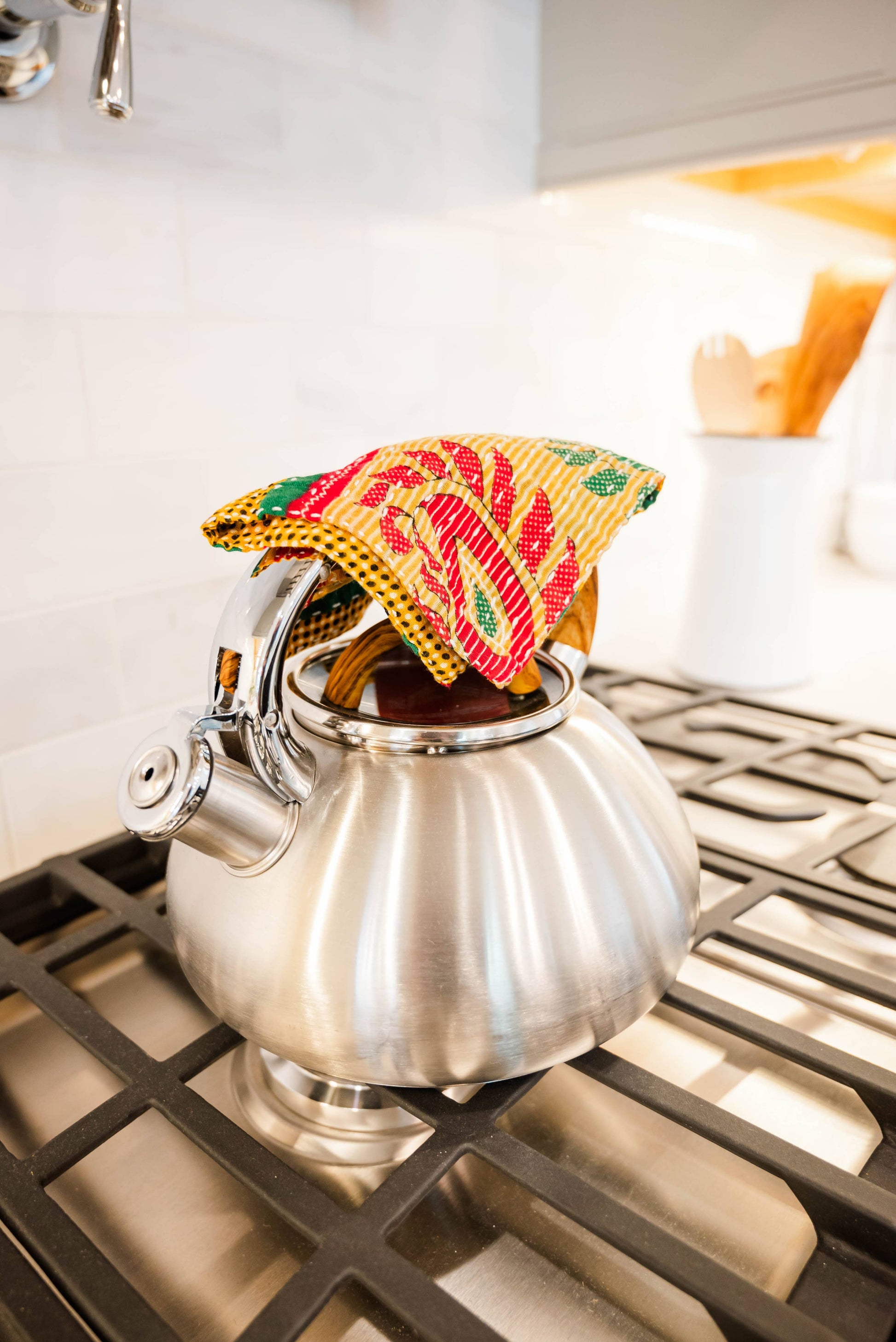 Silver teapot on a stove with a colorful tea cozy