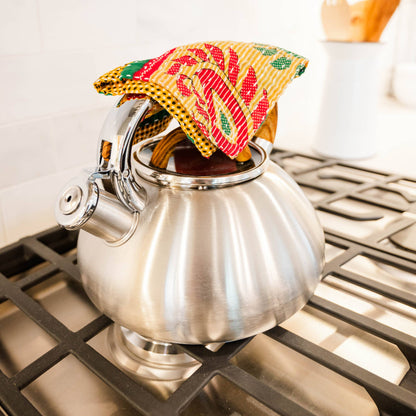 Silver teapot on a stove with a colorful tea cozy