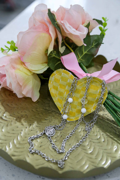 Necklace on a heart-shaped yellow gift pouch with pink flowers and green leaves