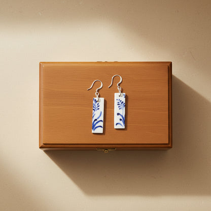 Pair of earrings with blue floral patterns on a wooden box with a light beige background