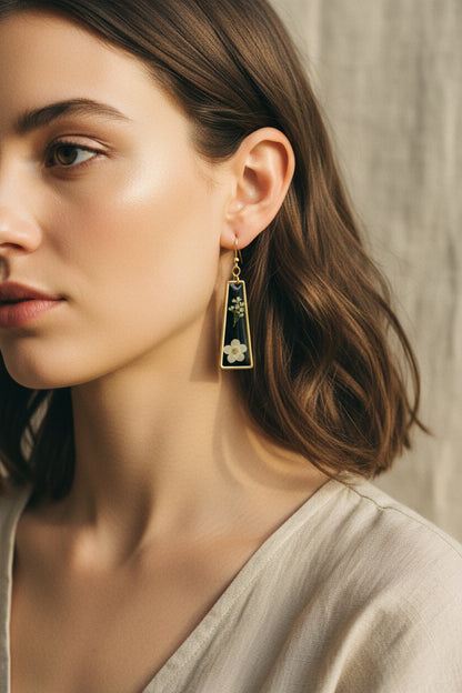 Gold earring with black triangle pendant featuring floral designs being worn against a neutral background