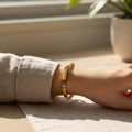 Colorful beaded bracelet with a gold detail bead being worn and showcased on a tabletop with a beige background