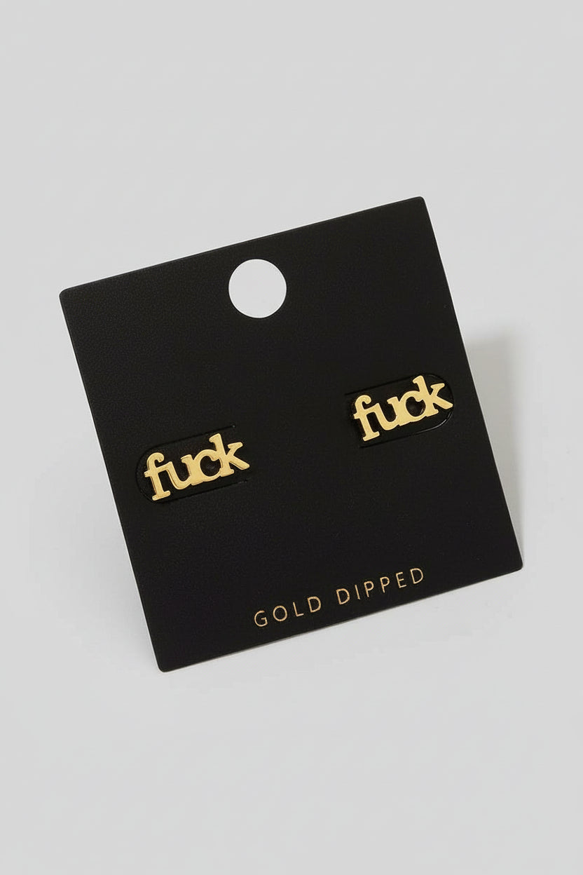 A pair of gold-dipped stud earrings with the word 'fuck' written in a stylized font, presented on a black backing card.