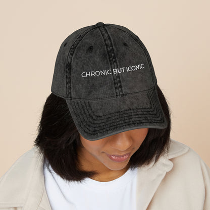 Person wearing a black cap with 'CHRONIC BUT ICONIC' text on a white background