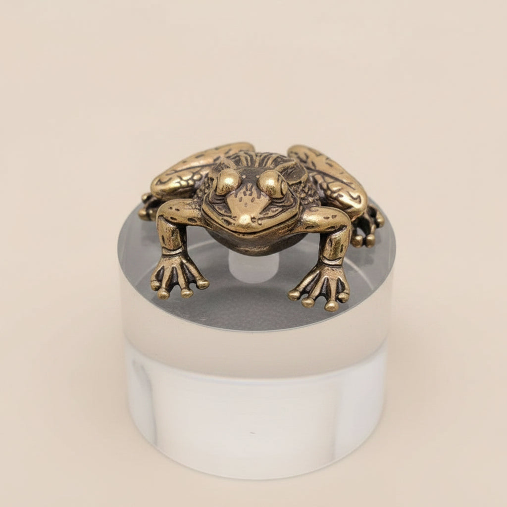 Bronze frog sculpture on a clear cylindrical stand against a gray background