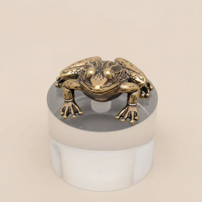 Bronze frog sculpture on a clear cylindrical stand against a gray background