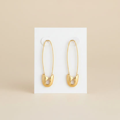 Gold safety pin earrings on a white backing card and a beige background