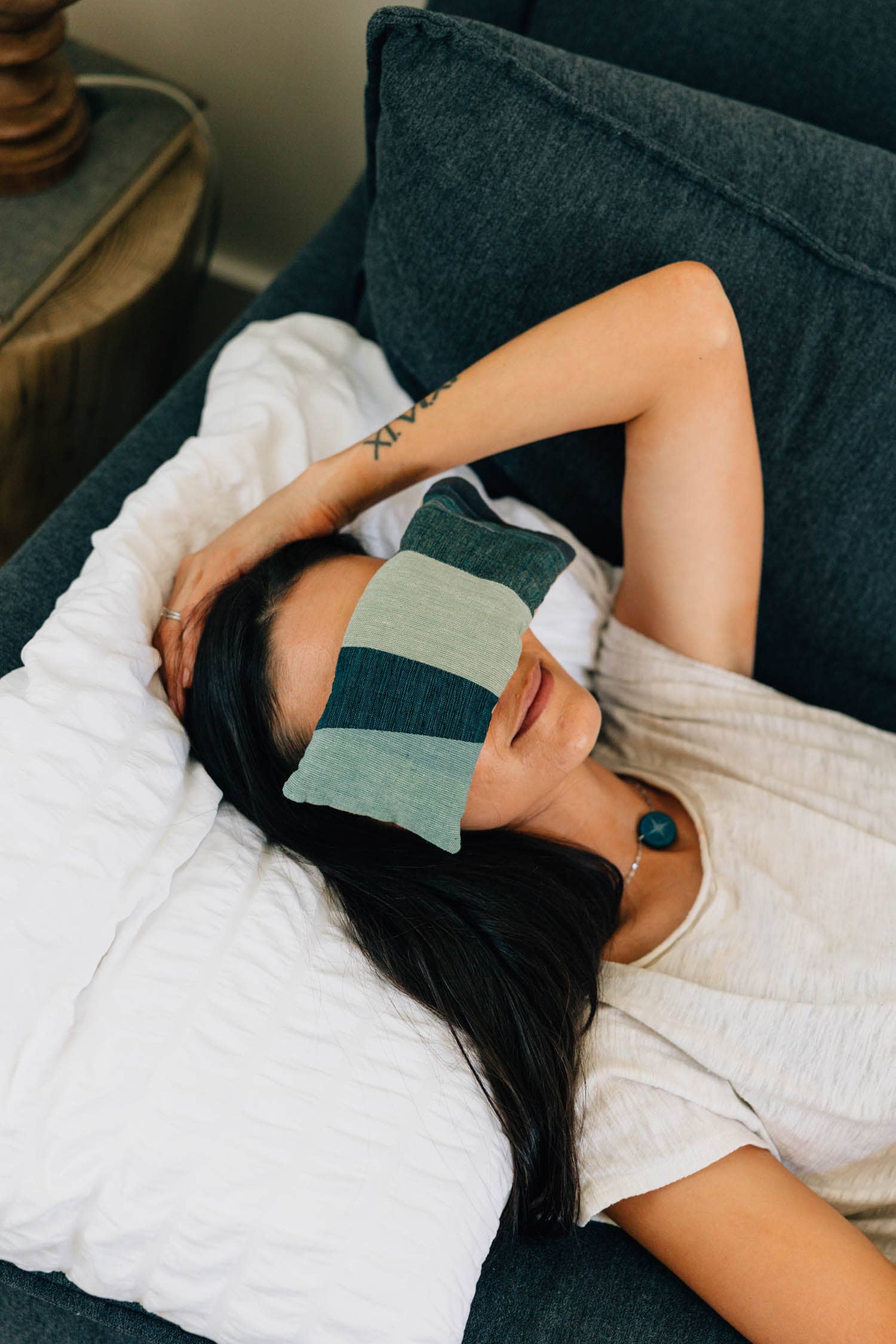 Woman lying on a couch with a green and gray striped eye mask on her eyes.