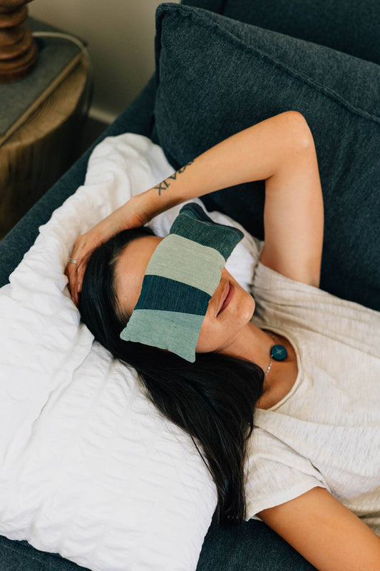 Woman lying on a couch with a green and gray striped eye mask on her eyes.