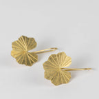 Close up view of the brass lotus leaf-shaped earrings on a light gray background