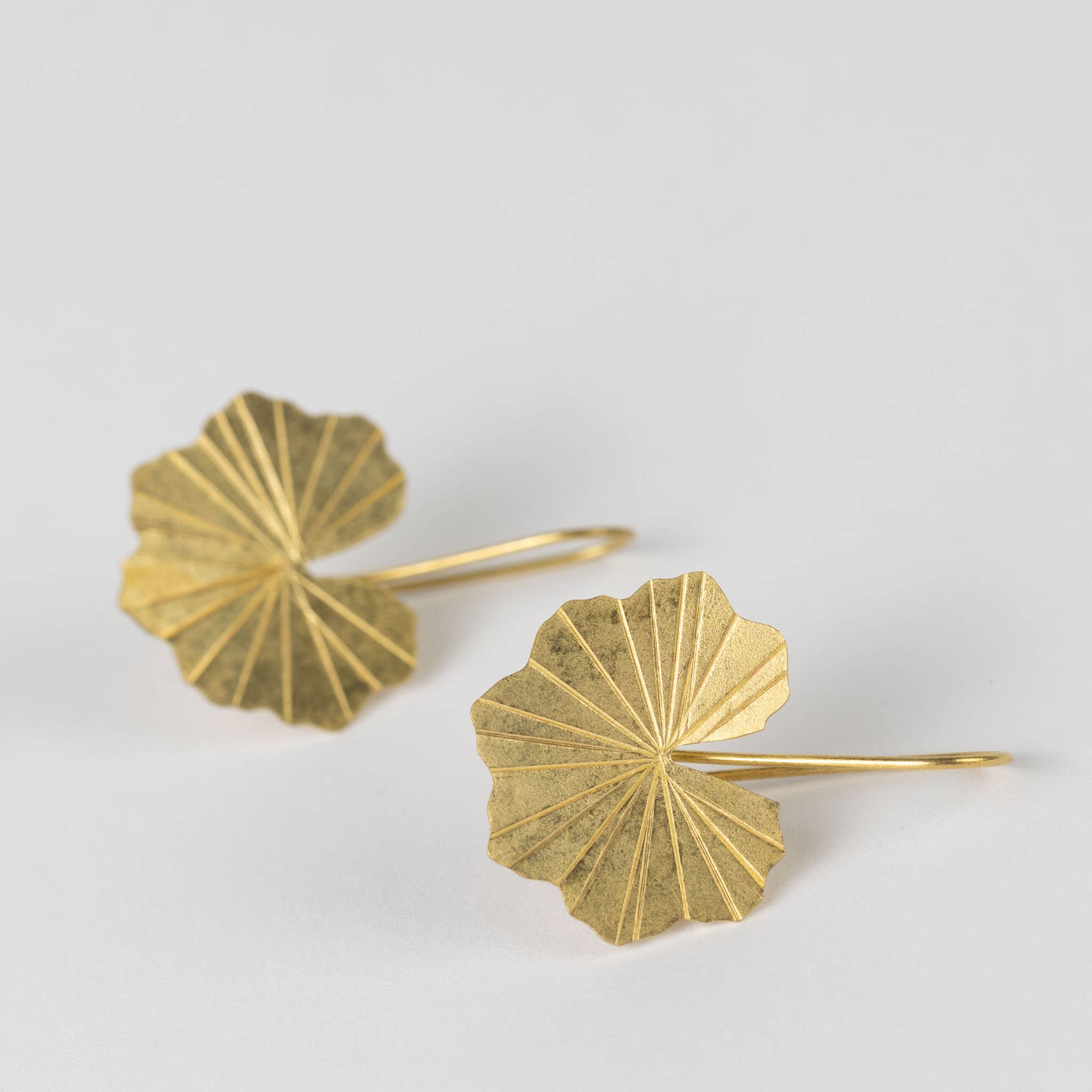 Close up view of the brass lotus leaf-shaped earrings on a light gray background