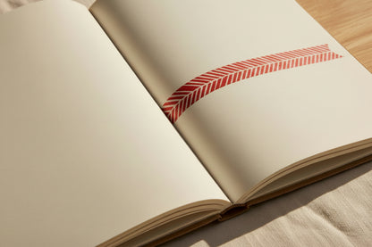 Close up of the red and white herringbone washi tape on a journal with a tabletop and natural textile in the bakground.