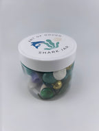 A 6oz jar containing blue playdough, a shark figurine, a faux plant, seashells, and gems, ideal for sensory play."