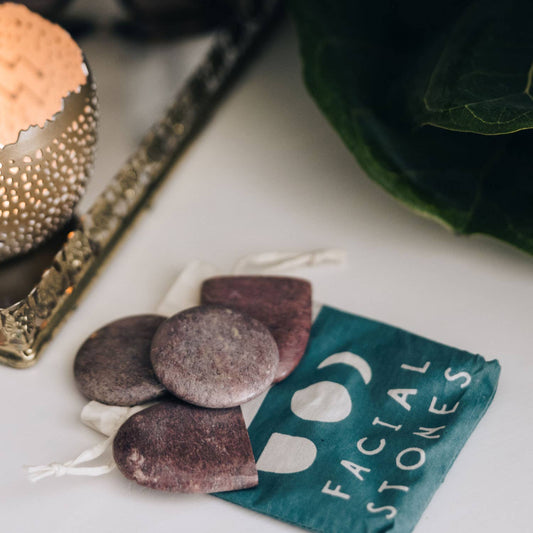 Facial stones and a green pouch labeled 'Facial Stones' on a white surface.