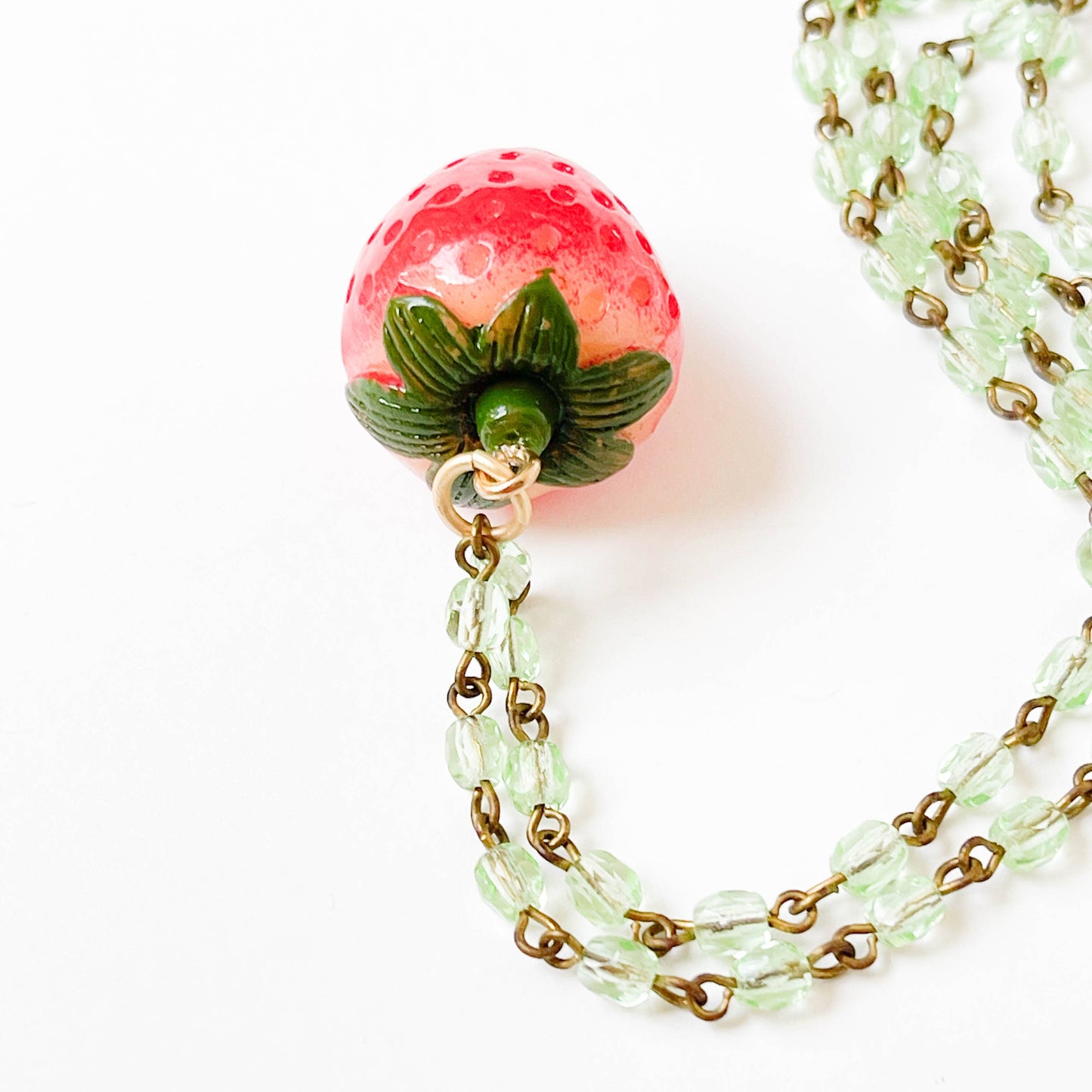 Detailed close-up of resin strawberry pendant, green bead chain, and matching green tassel