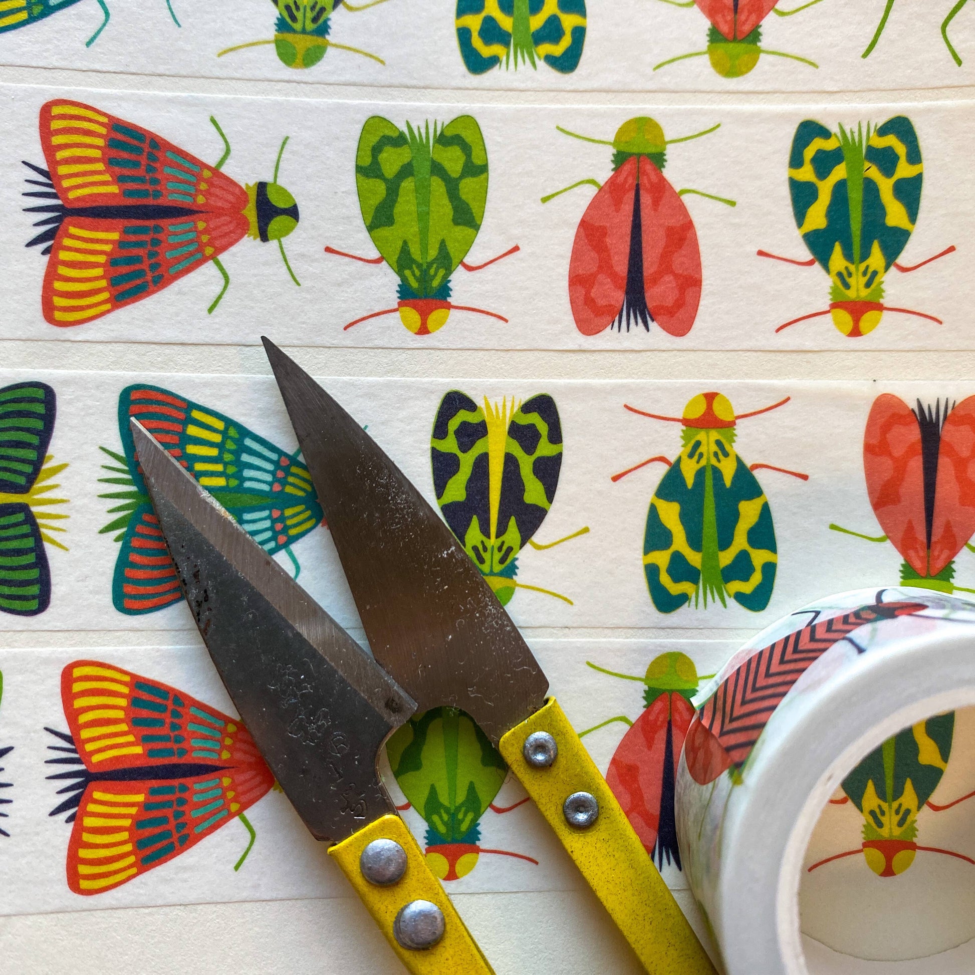 Close up image of Mondo Bug washi tape unrolled and next to scissors