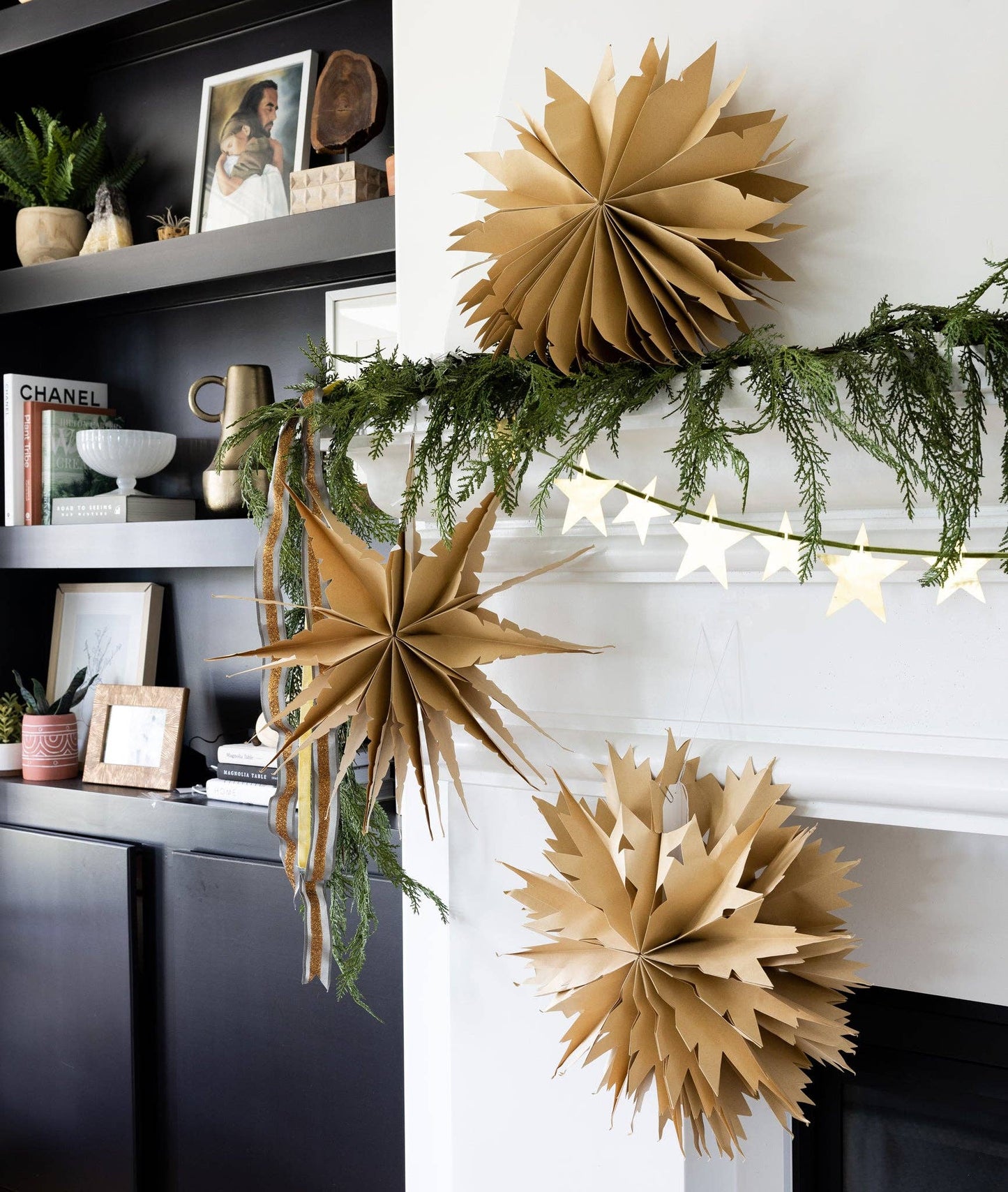 Decorative paper stars on a mantelpiece with greenery and string lights.