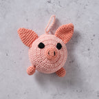 Close up of the crocheted pink pig tape measure on a concrete surface