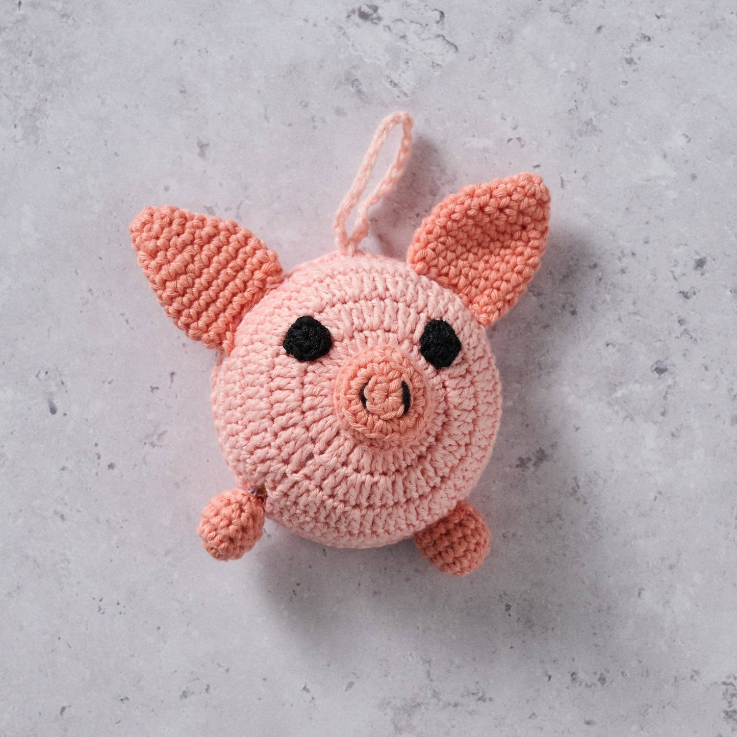 Close up of the crocheted pink pig tape measure on a concrete surface