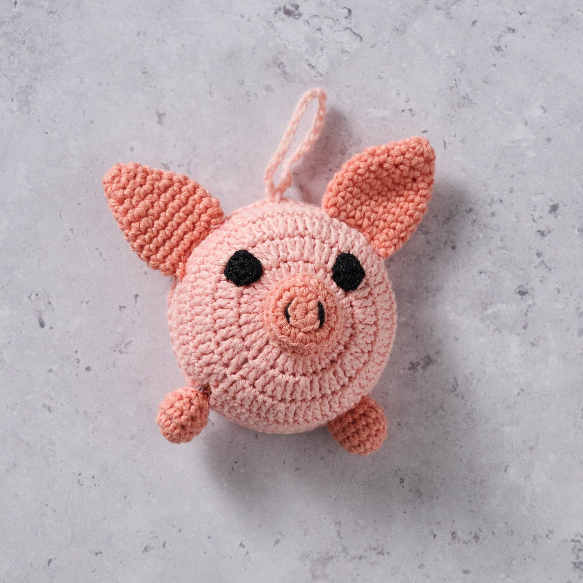Close up of the crocheted pink pig tape measure on a concrete surface