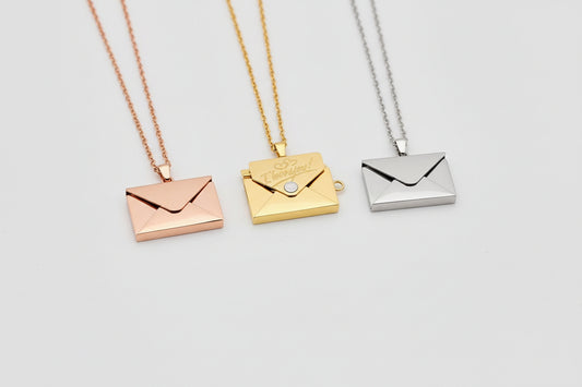 Three gold and silver envelope-shaped pendants on a hand.