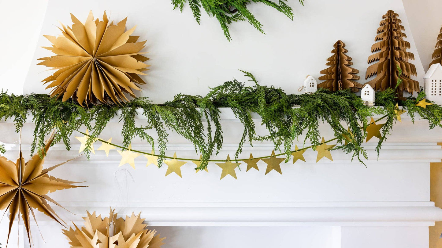 Decorative mantel with greenery, gold paper stars, and festive trees.