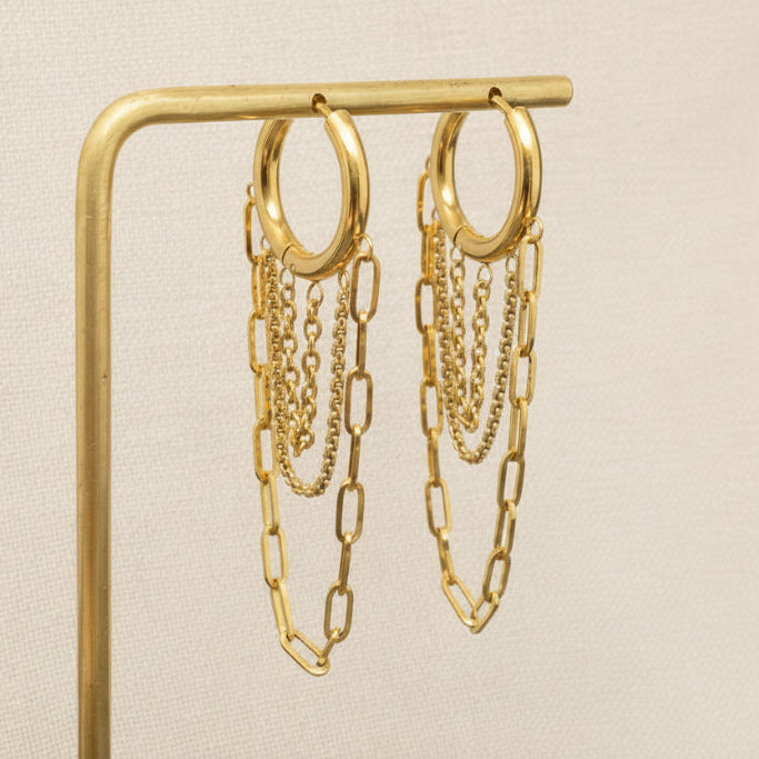 Gold chain earrings on a gold stand against a beige background