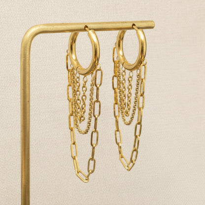 Gold chain earrings on a gold stand against a beige background