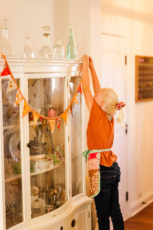 Mini pennant garland styled above a crib or playroom nook with cozy, colorful decor