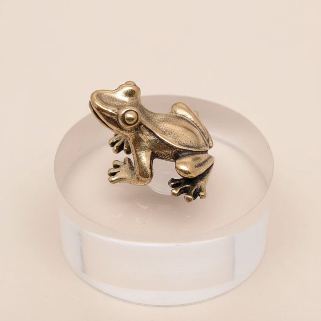 A brass frog figurine on a clear crystal ball against a gray background
