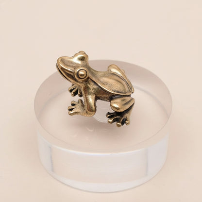 A brass frog figurine on a clear crystal ball against a gray background