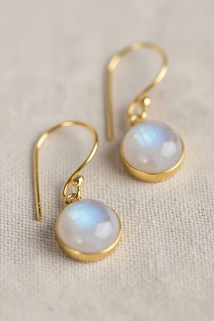 Close-up of moonstone earrings reflecting soft white shimmer on a light beige linen background