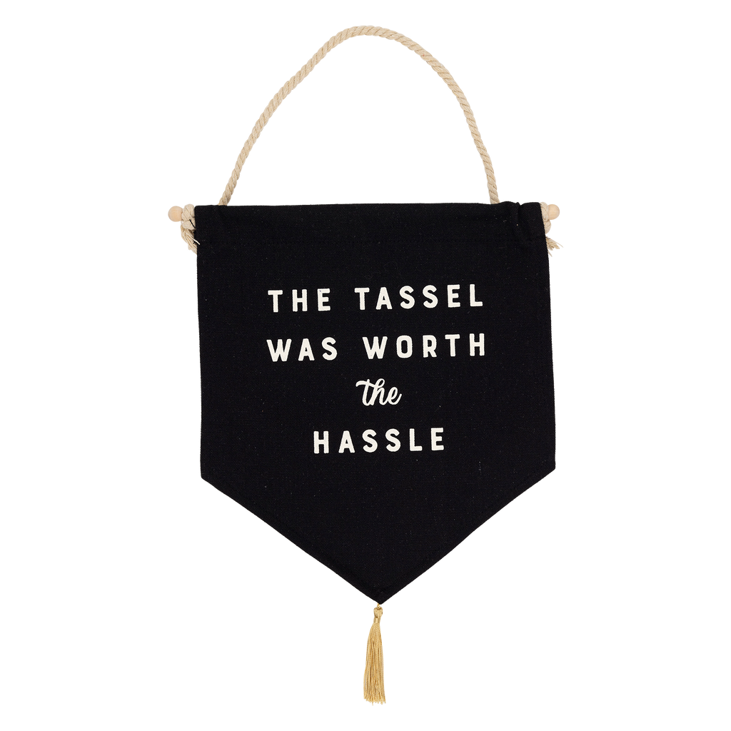 Close up of the Graduation canvas banner with "The Tassle Was Worth the Hassle" text, wood dowel, and gold tassel