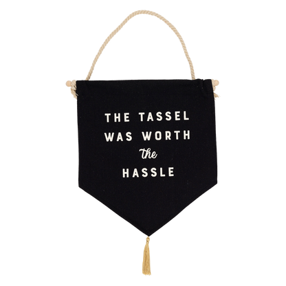 Close up of the Graduation canvas banner with "The Tassle Was Worth the Hassle" text, wood dowel, and gold tassel