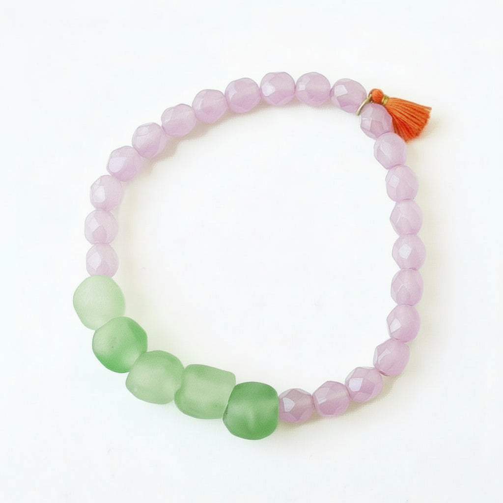 A pink and green beaded bracelet with a red tassel, displayed in a flower-like pattern.