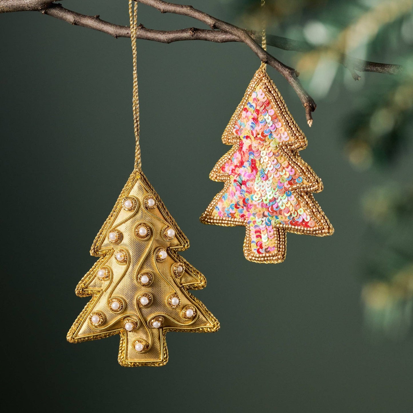 Two Christmas tree-shaped ornaments, one gold and one multicolored, hanging from a branch.