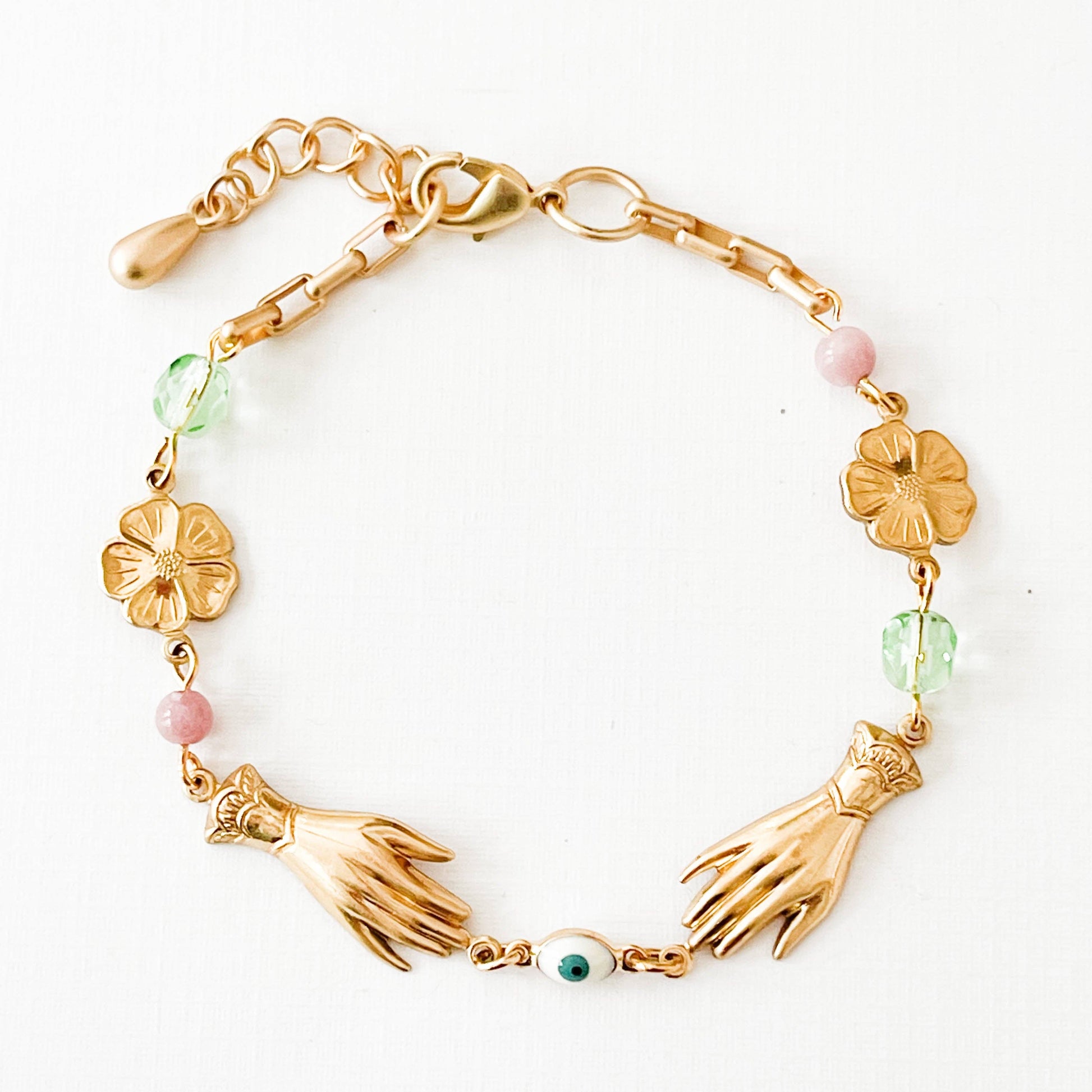 Close-up of pastel charm bracelet with gold floral accents on linen backdrop