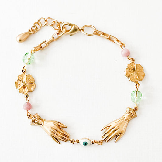 Close-up of pastel charm bracelet with gold floral accents on linen backdrop