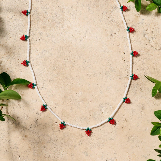 Delicate white glass bead necklace with red and green strawberry motif, hand-beaded on a stone surface