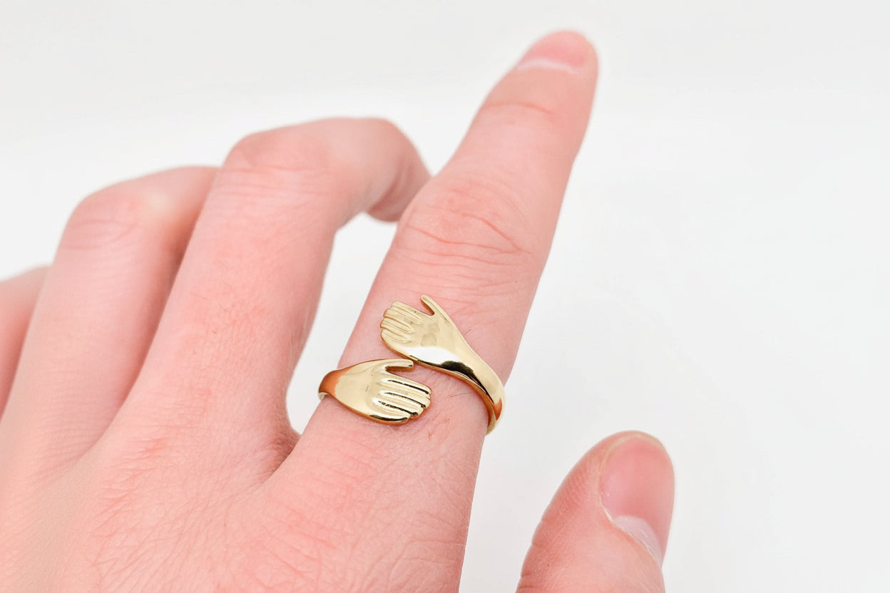 Gold hand-shaped ring on a finger against a white background